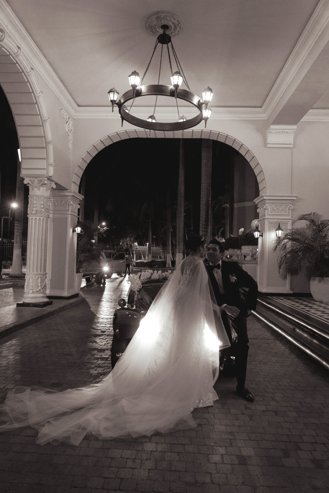 Novios bajo arco iluminado en blanco y negro
