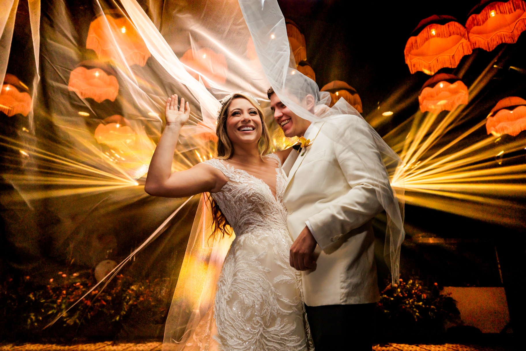 Novios celebrando con velo al viento bajo luces cálidas